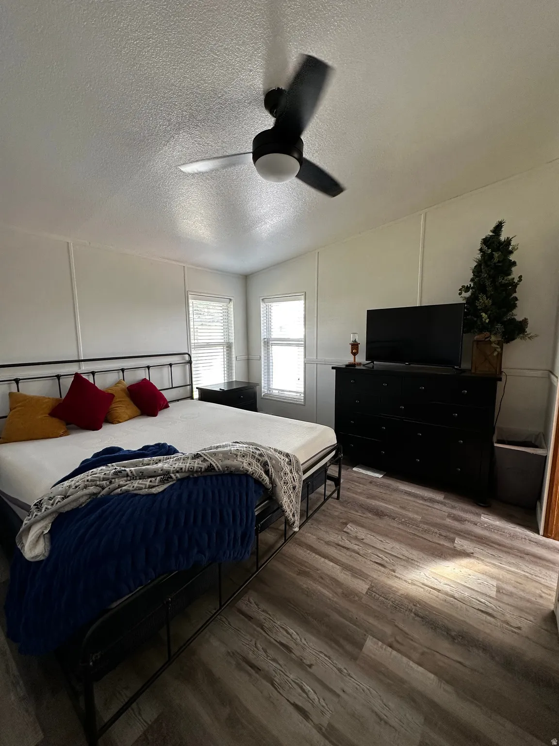 Spacious room featuring wood-finish flooring, a vaulted ceiling, and a ceiling fan with integrated lighting