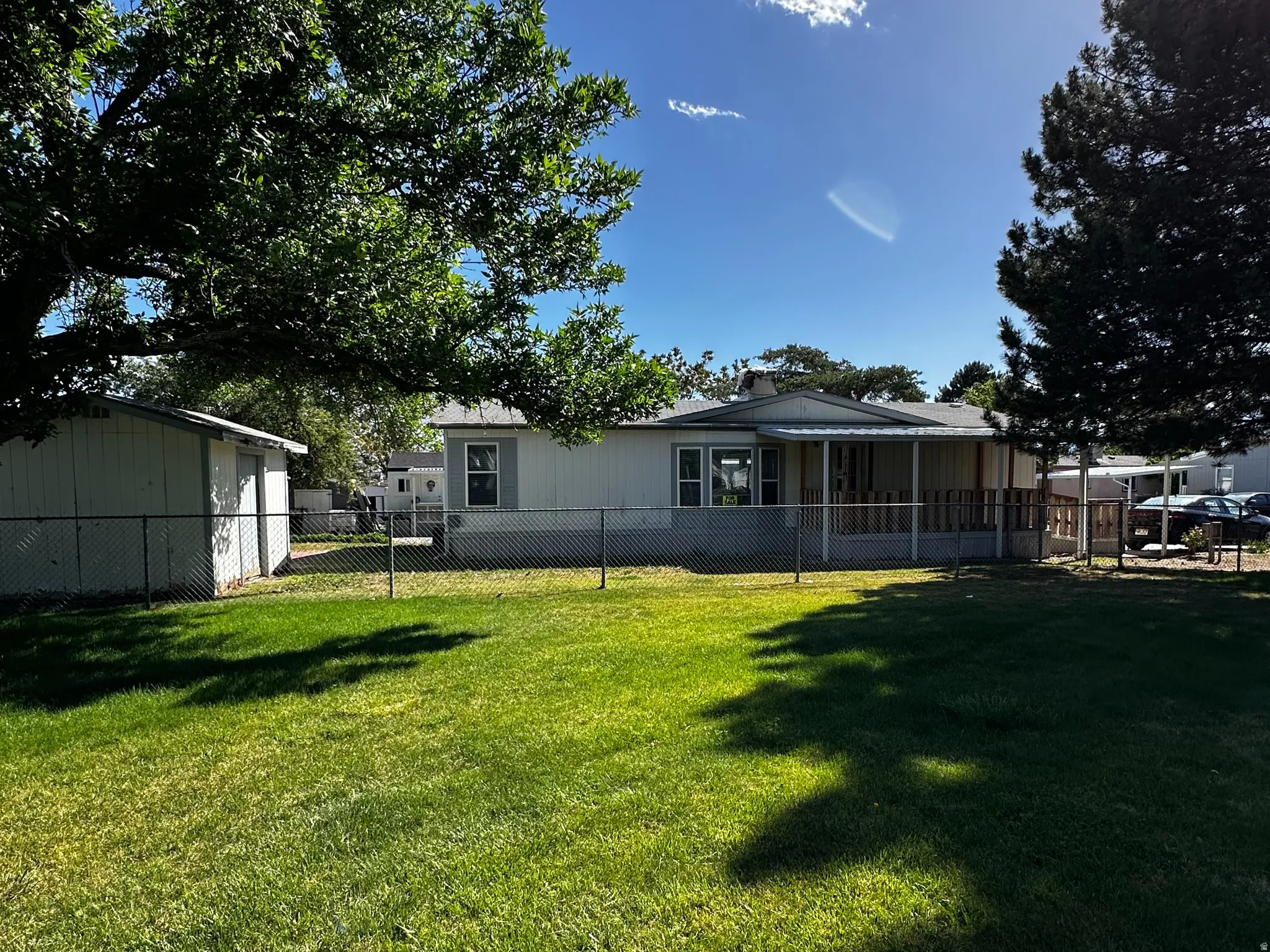 Expansive lawn area featuring a chain-link fence, mature trees, and a storage shed