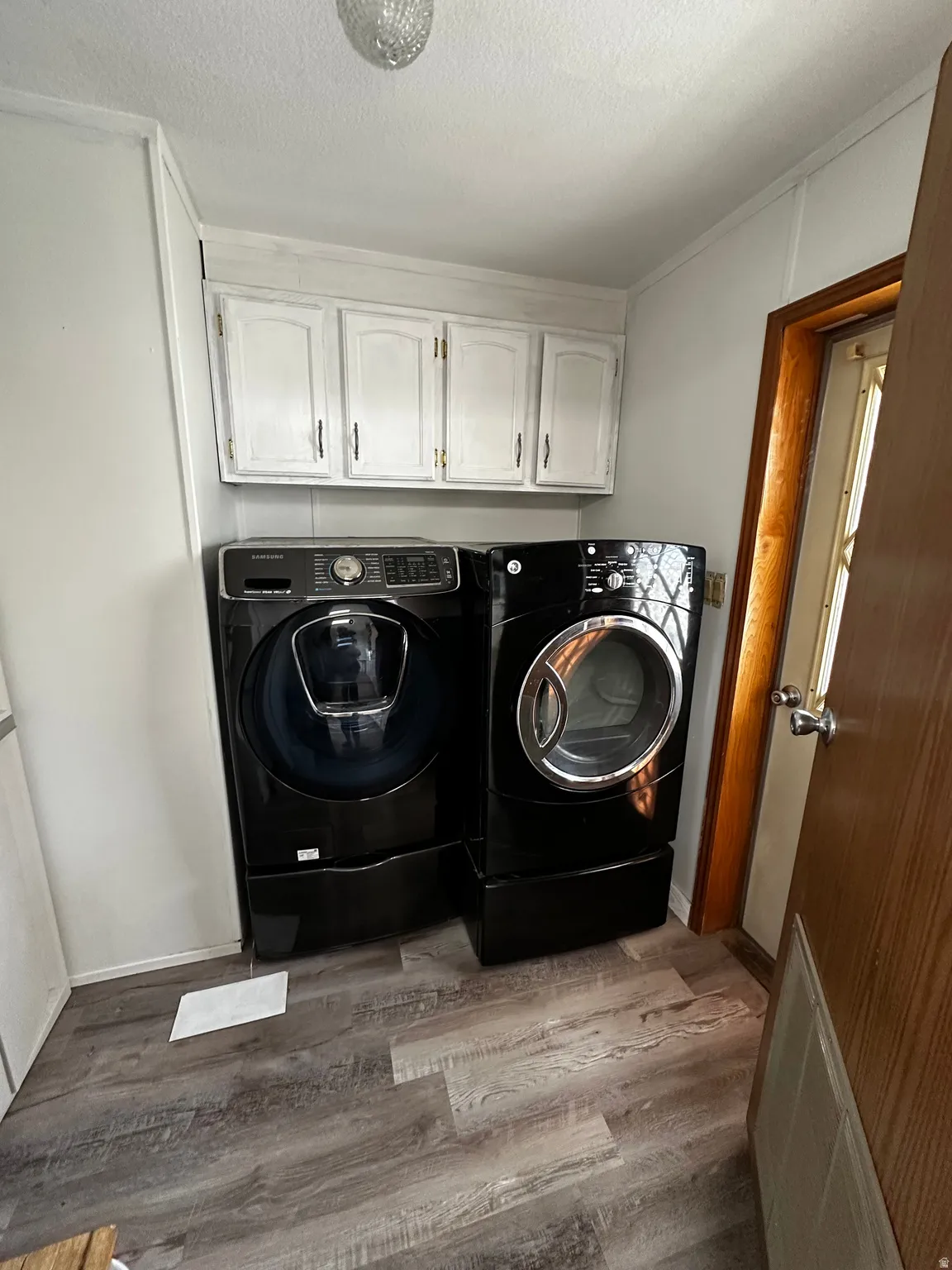 Utility area featuring wood-finish flooring and upper cabinetry with brass-toned hardware