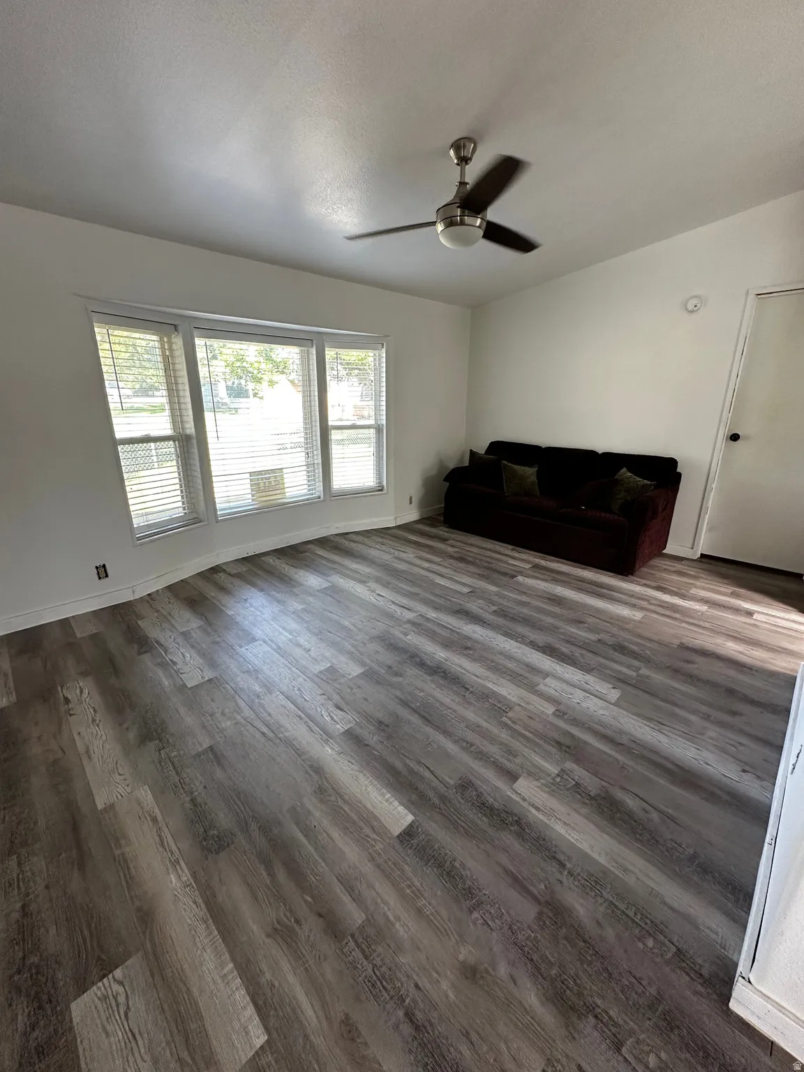 Spacious room featuring multi-pane windows with blinds, wood-finish flooring, and a ceiling fan with integrated lighting
