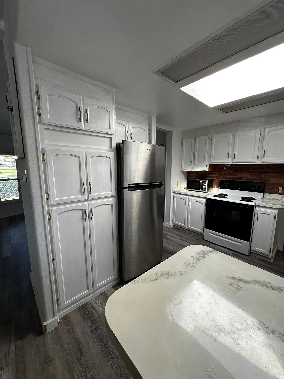 Kitchen featuring white cabinetry, a stainless steel refrigerator, a built-in electric range with an overhead microwave, a red brick-patterned backsplash, and wood-finish flooring