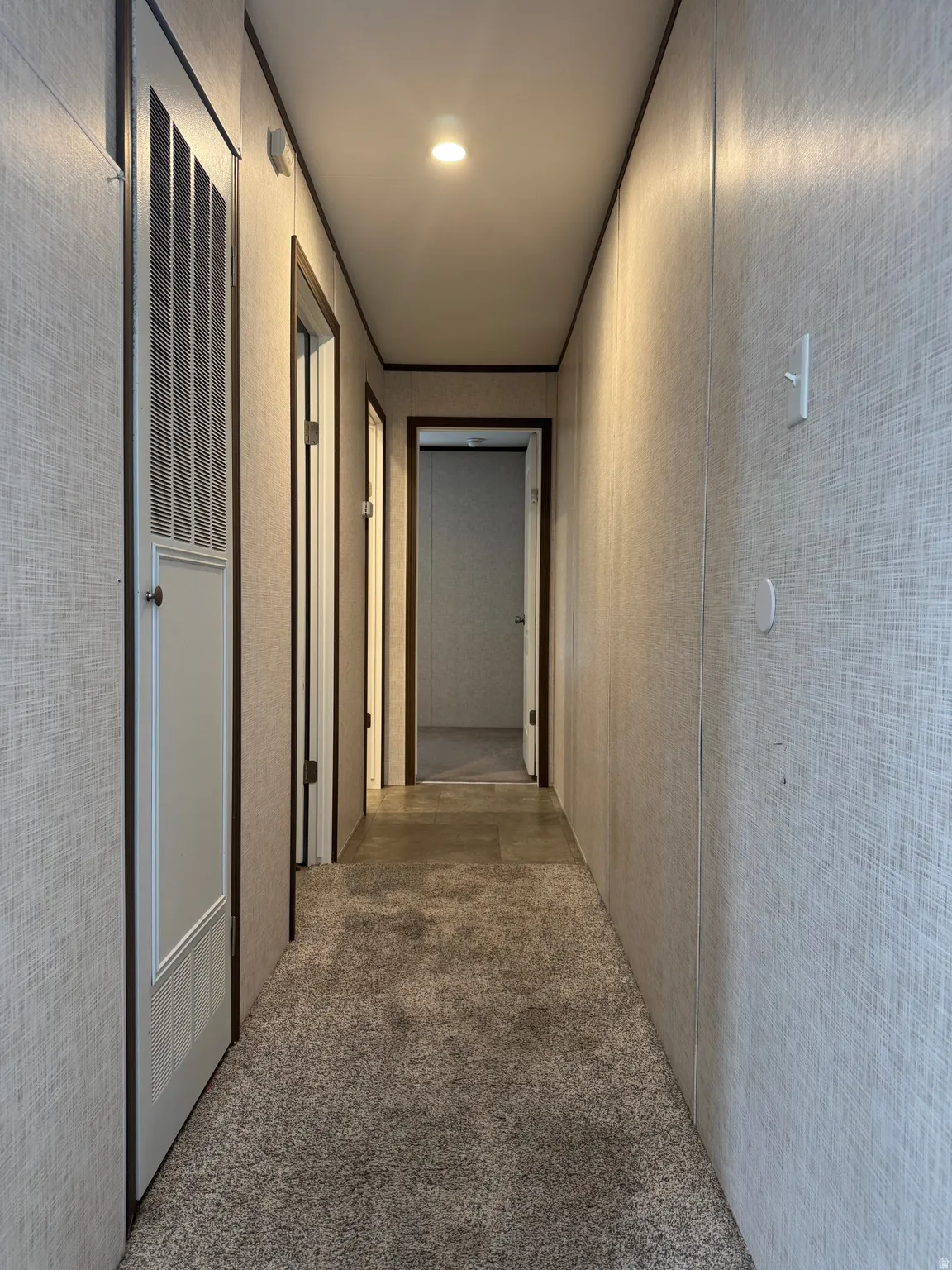 Carpeted hallway featuring textured wall panels and recessed lighting