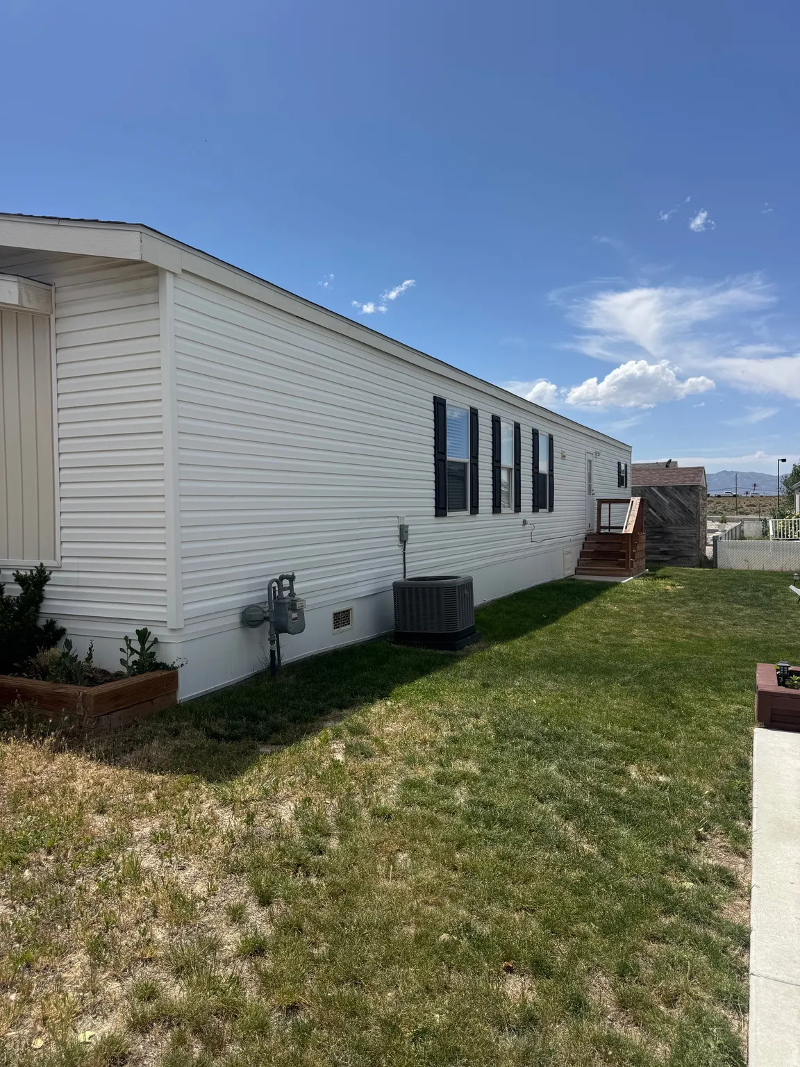 White siding exterior with black window shutters, a wooden entry deck, and a grass area