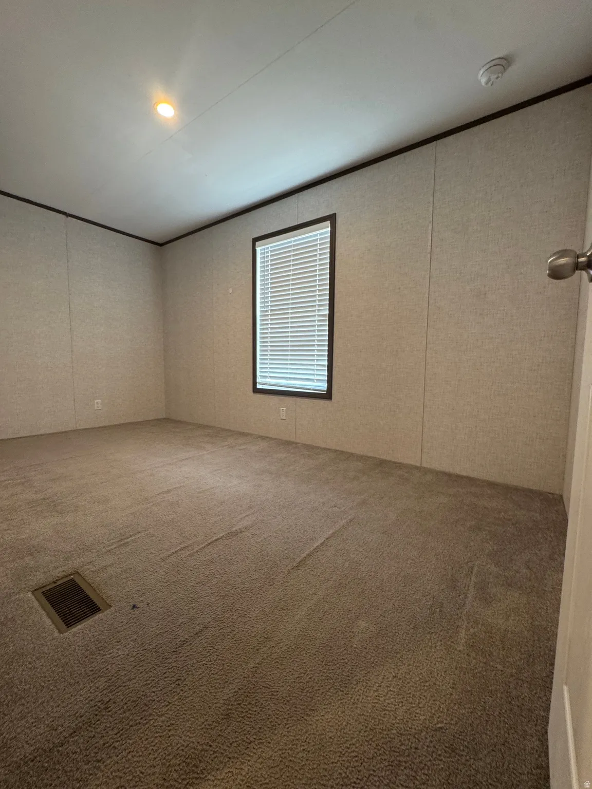 Carpeted room featuring a single window with blinds, recessed ceiling lighting, and a wall-mounted smoke detector