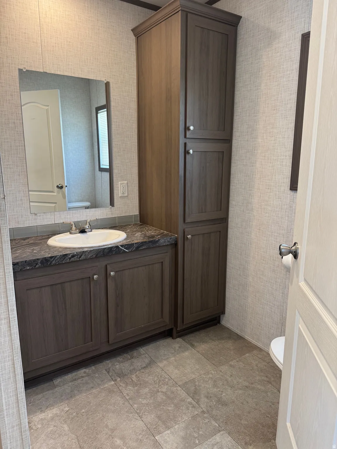 Bathroom vanity featuring a single basin sink, dark countertop, and wood-finish cabinetry
