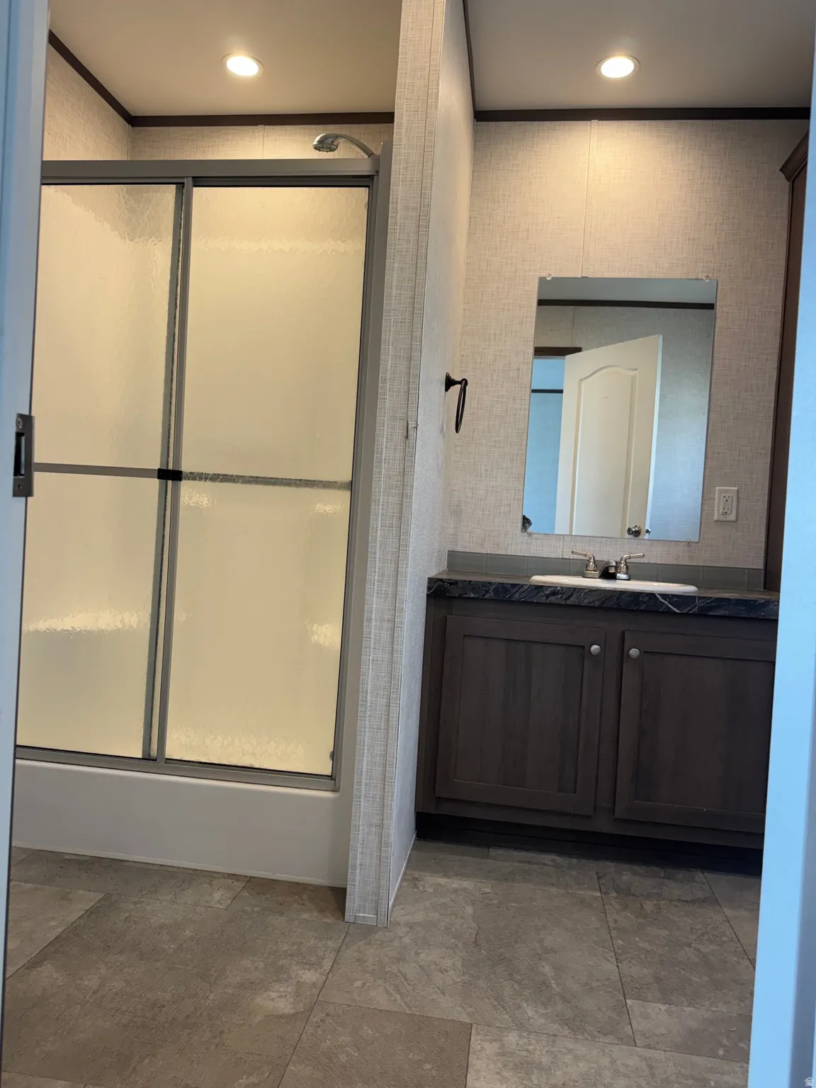 Bathroom featuring a shower-tub combination with frosted sliding glass doors, a single vanity with dark wood-finish cabinetry, a grey countertop, and a rectangular mirror
