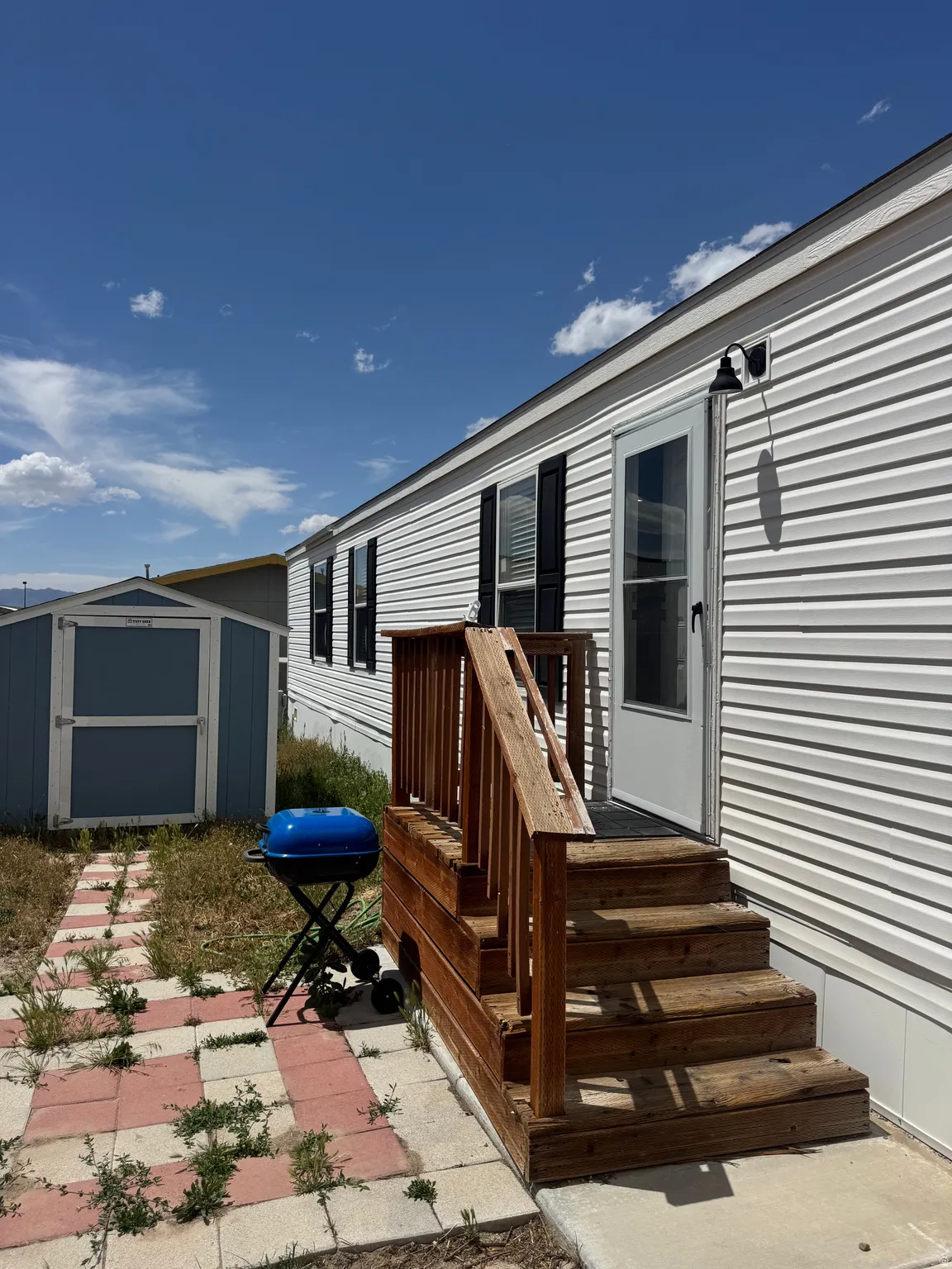 White horizontal siding exterior with black window shutters and a blue storage shed
