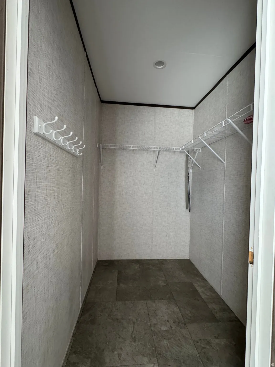 Spacious closet featuring durable tile-look flooring, neutral textured wall panels, white wire shelving, and a multi-hook rack