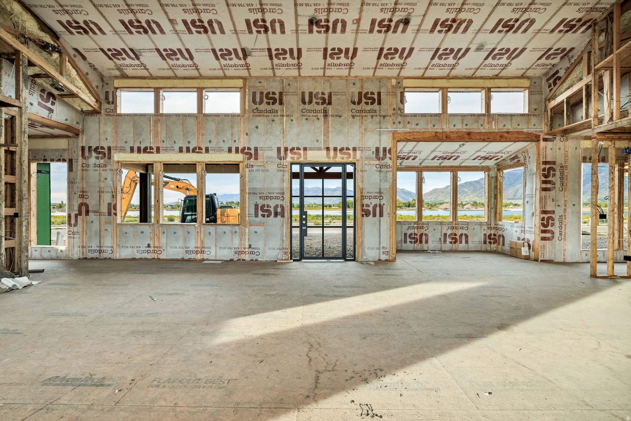 Expansive interior space under construction, featuring multiple large window openings, a framed door opening, and visible structural framing