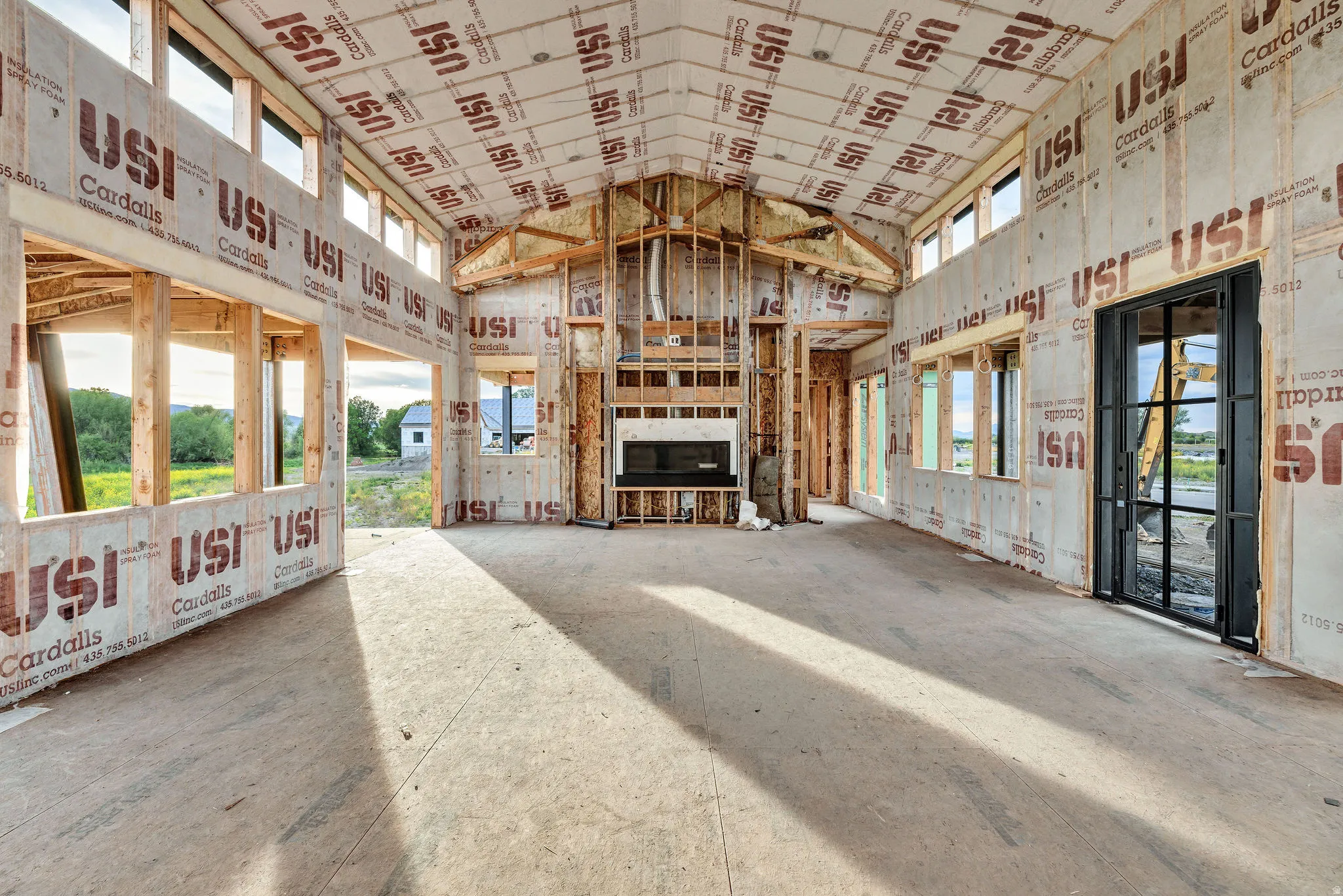 Spacious unfinished room featuring a vaulted ceiling with exposed framing, an integrated fireplace unit, and a black-framed glass door