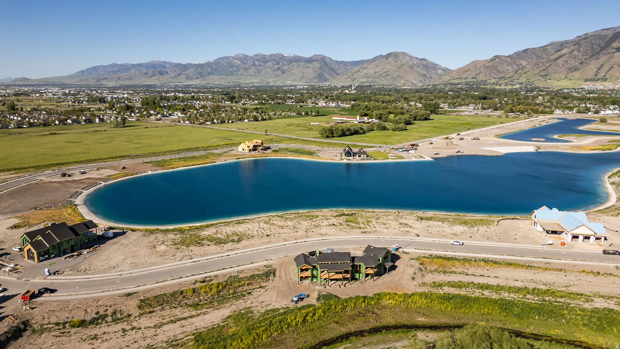 Expansive residential development featuring a large blue water body, multiple construction sites for residential structures, and paved roadways