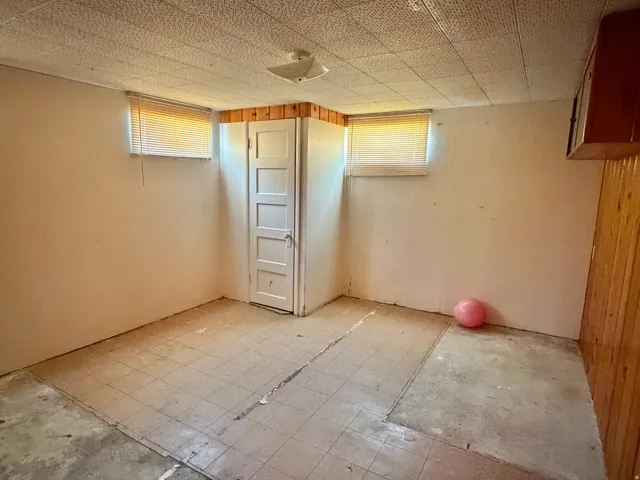 Room featuring a paneled interior door, two windows with blinds, wood paneling accents, and a textured ceiling
