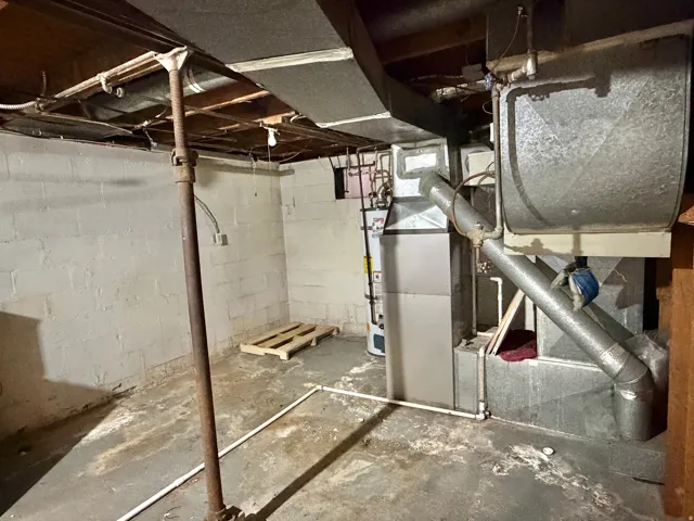 Utility room featuring a water heater, furnace, exposed ductwork, exposed ceiling joists, and concrete block walls