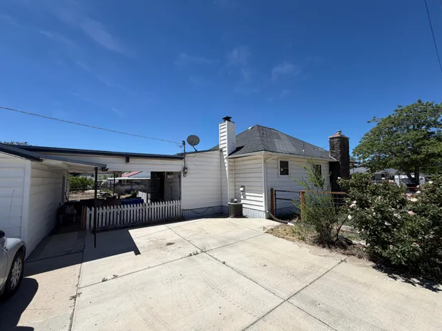 Concrete patio area featuring a white picket fence, a covered carport, and a stone-clad chimney