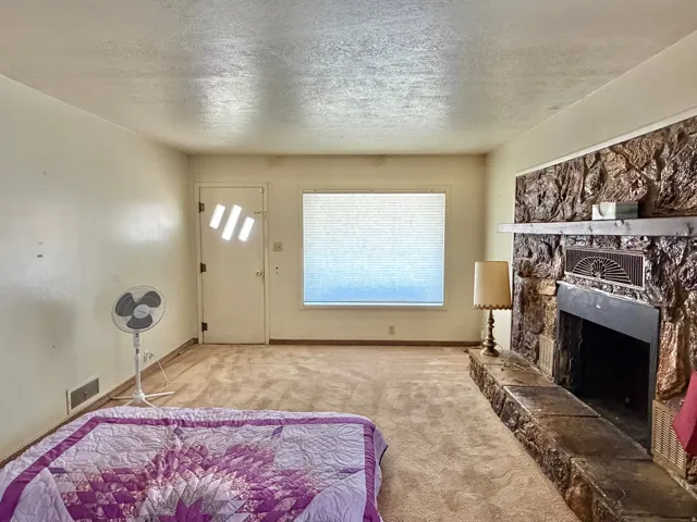Living area featuring a stone-clad fireplace with a hearth, a window with blinds, and light-toned wall finishes