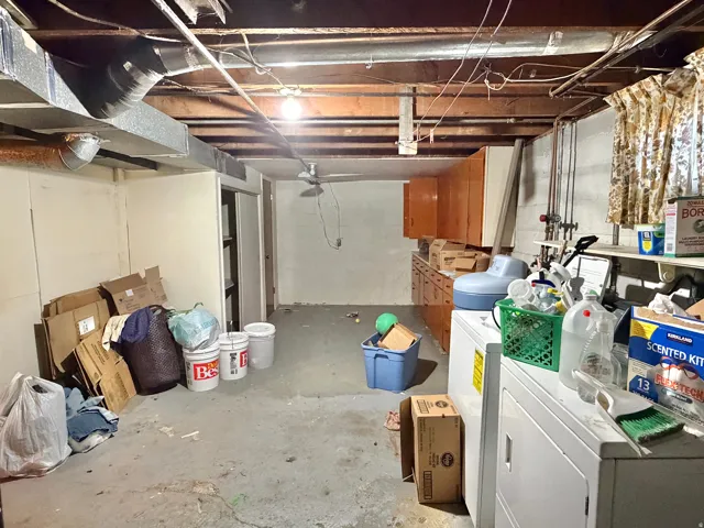 Unfinished basement with exposed ceiling joists and ductwork, featuring a utility sink, built-in cabinetry, and concrete flooring