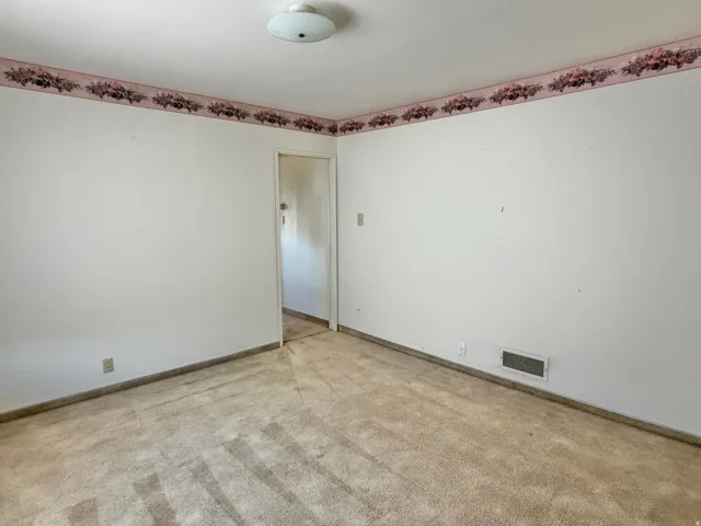 Carpeted interior room with white walls, baseboards, and a floral wallpaper border