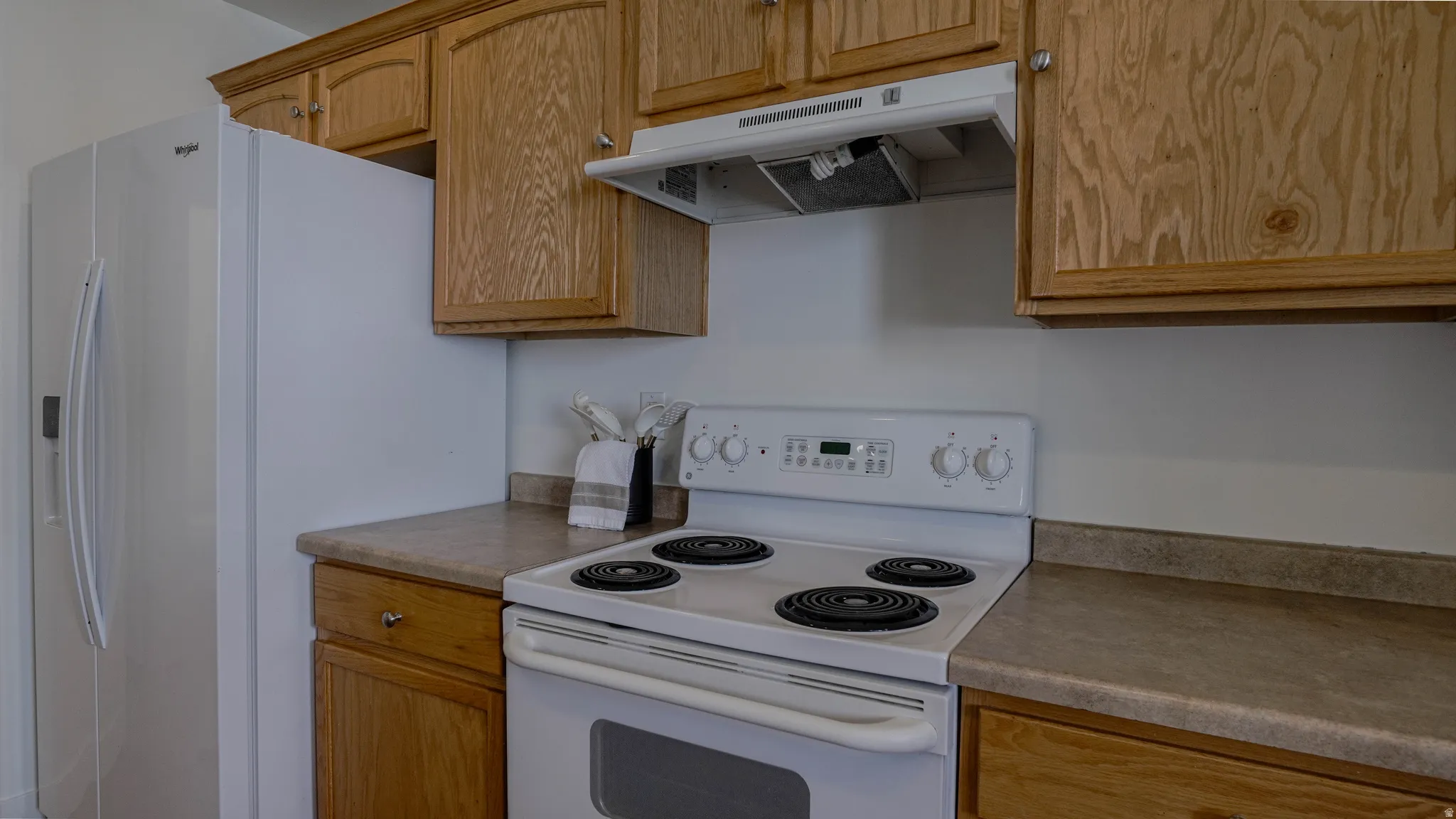Kitchen featuring wood cabinetry, laminate countertops, a white electric range, and a white refrigerator