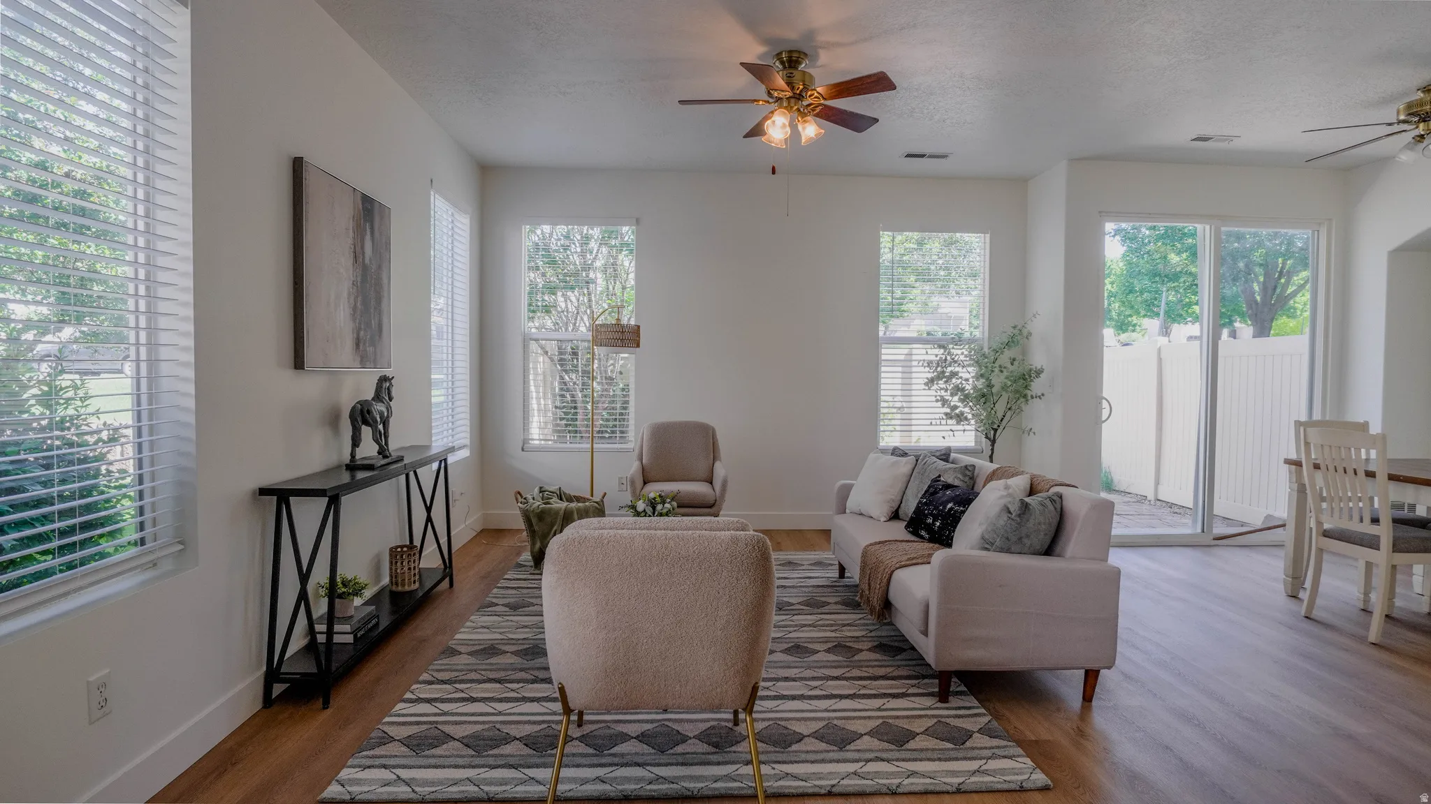 Open-concept living area featuring wood-finish flooring, multiple windows with blinds, and white walls