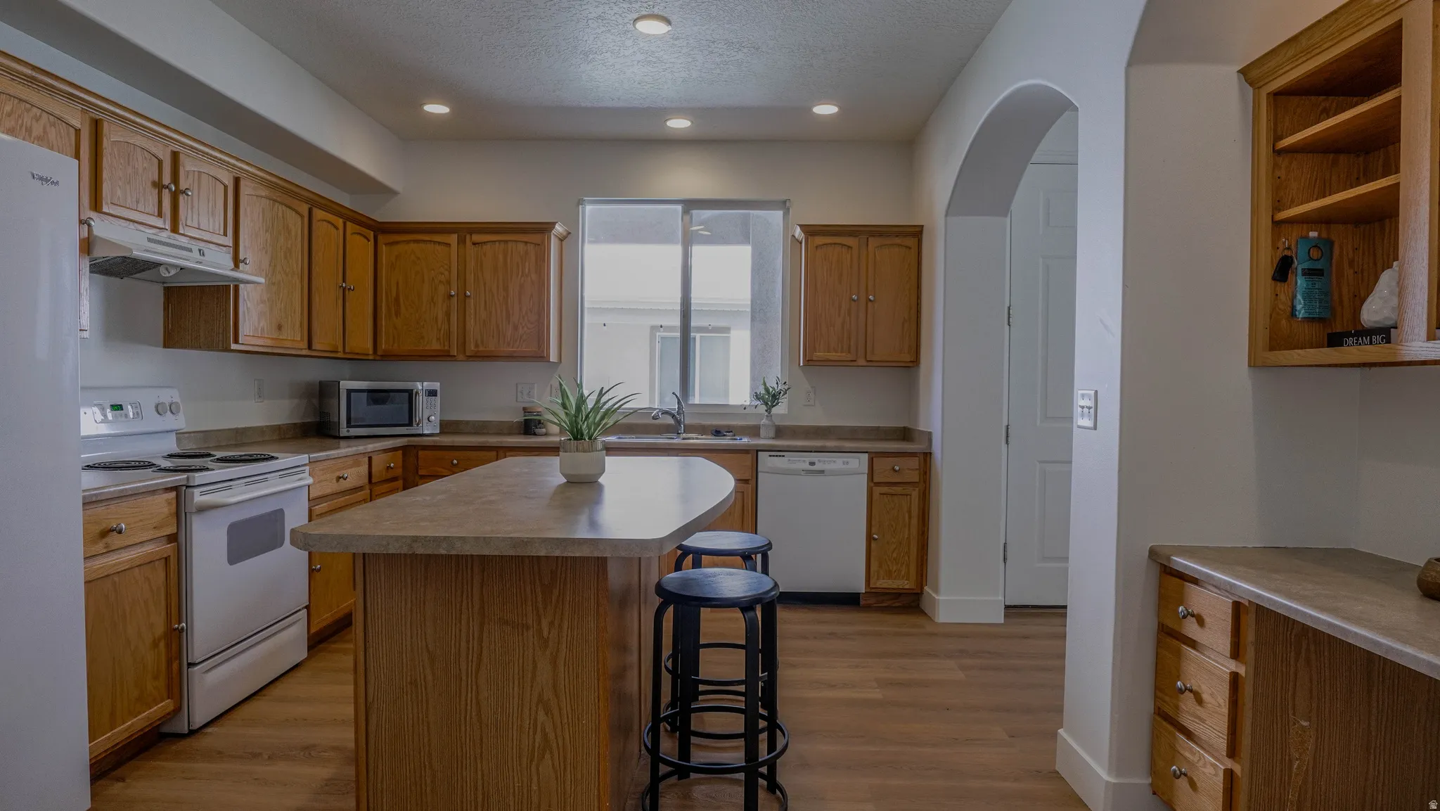 Kitchen featuring wood-finish cabinetry, white appliances, and a central island with an integrated breakfast bar