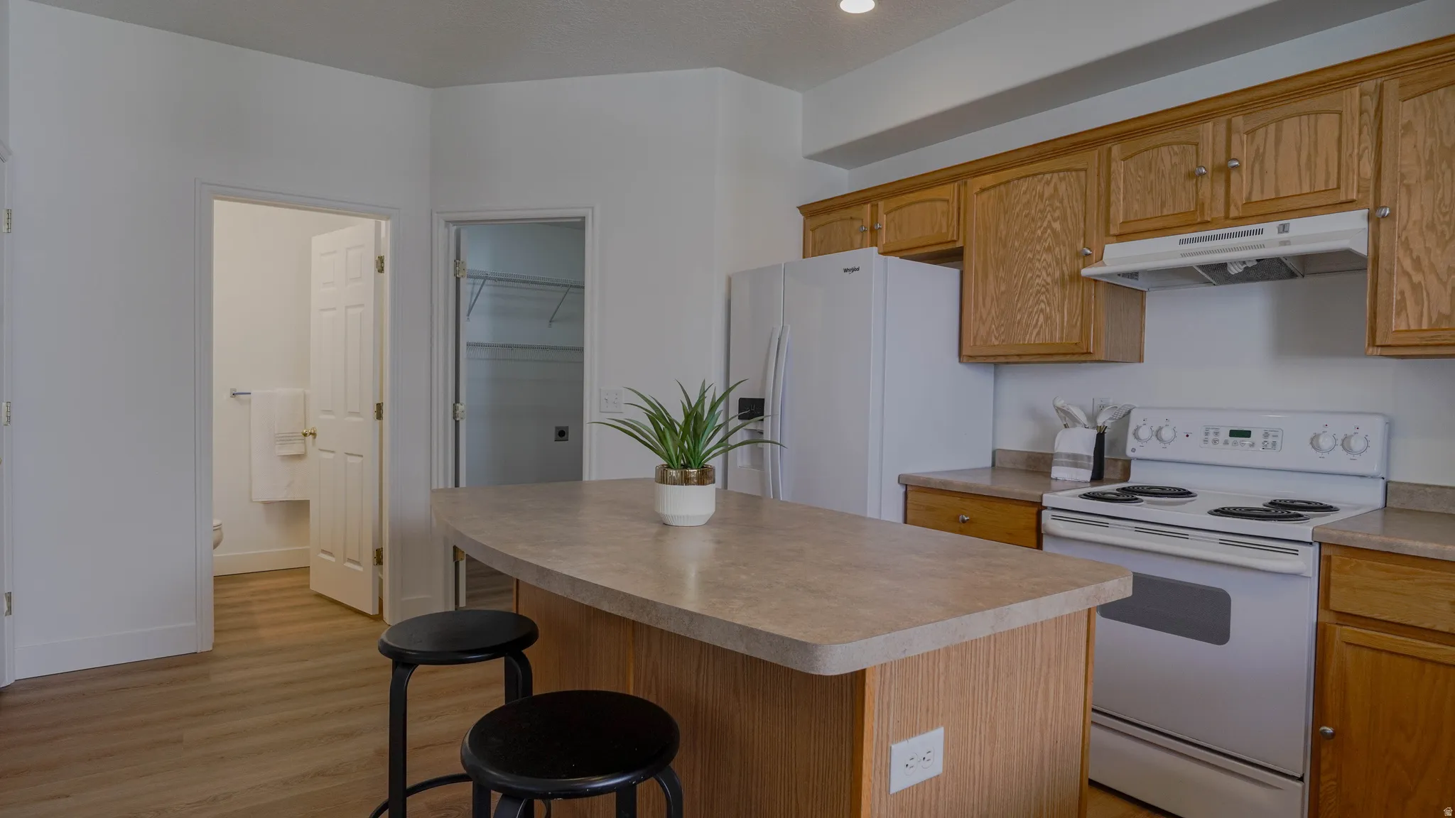 Kitchen featuring wood-finish flooring, a central island with countertop seating, wood cabinetry, a white range, and a white refrigerator