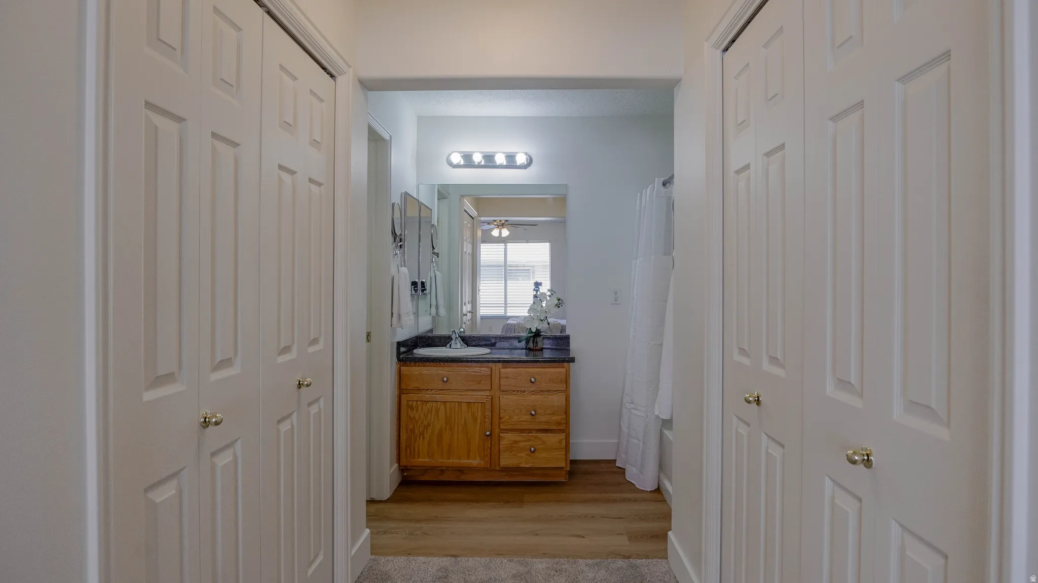 Hallway featuring two-panel bifold closet doors with brass knobs, leading to a bathroom with a wood-finish vanity, dark countertop, and integrated sink