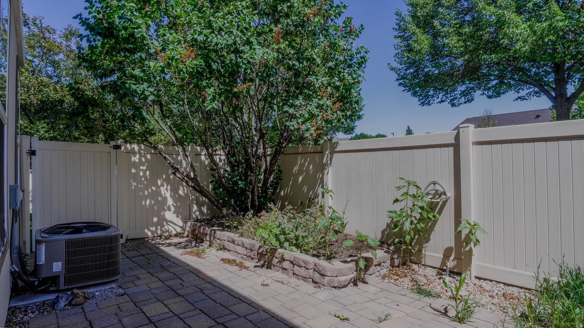 Private patio featuring paver stones, a raised garden bed with stone retaining wall, and a light-toned privacy fence