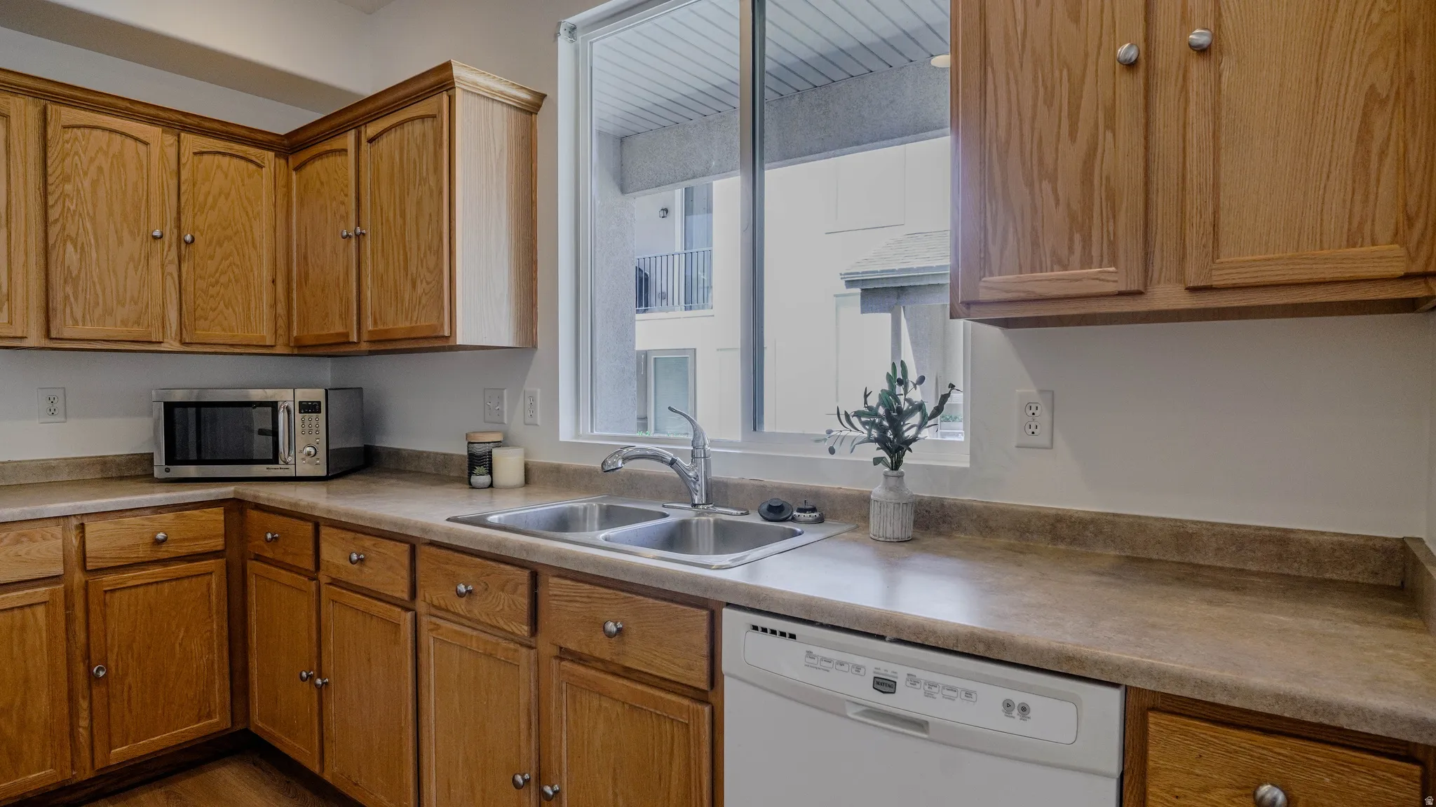 Kitchen featuring wood cabinetry, laminate countertops, a double basin stainless steel sink with a chrome faucet, and a white dishwasher