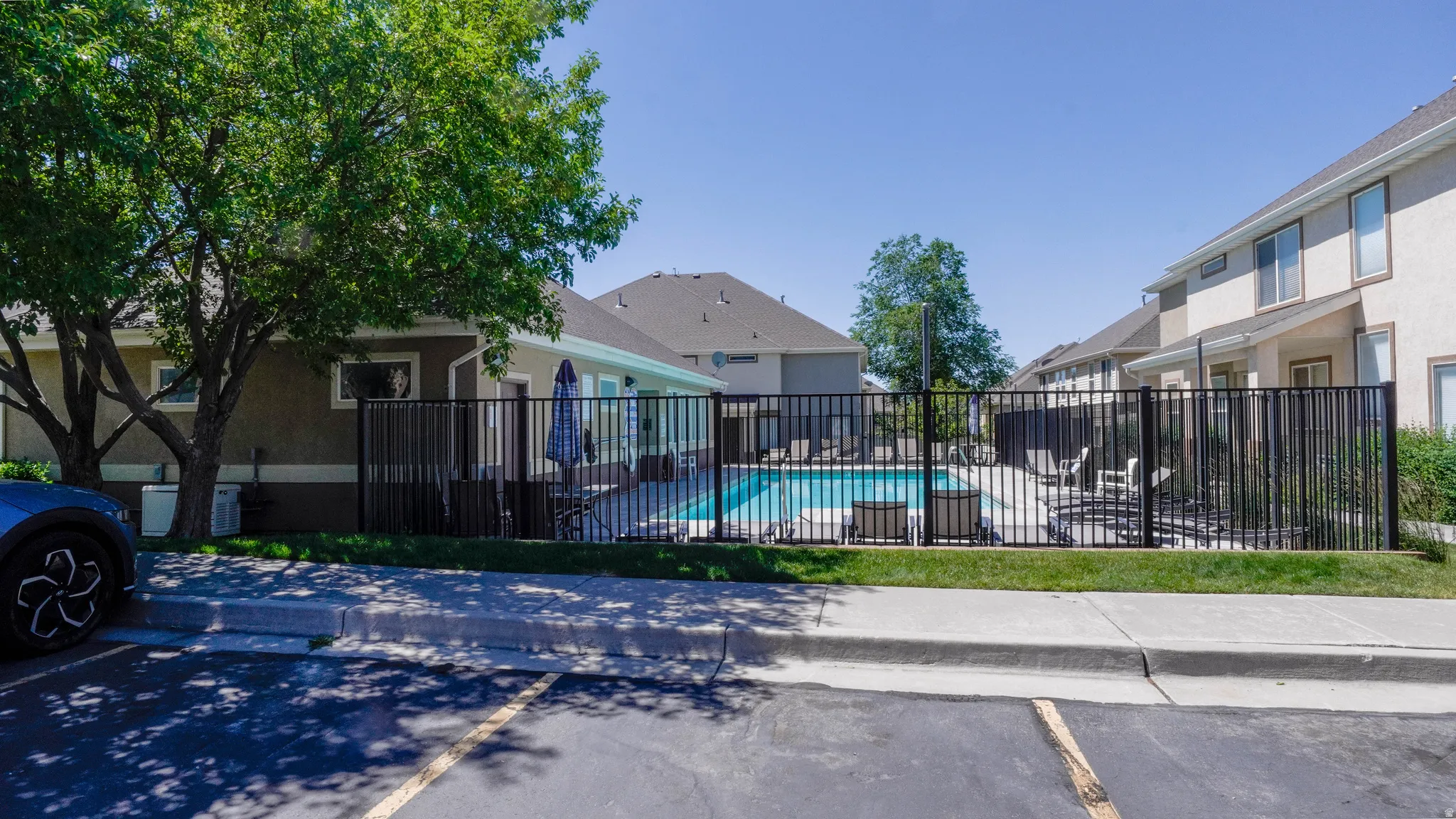 Community swimming pool with surrounding black metal fencing, a concrete pool deck, and integrated spa