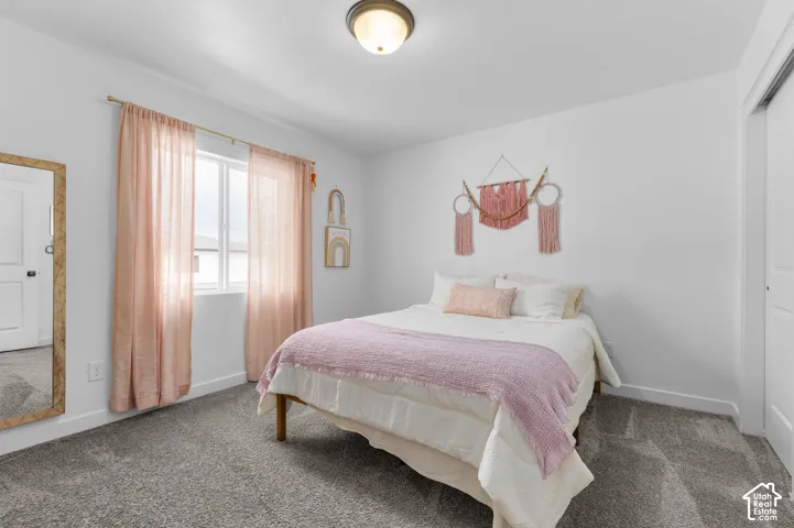 Bedroom featuring a window with sheer curtains, neutral gray carpet, and a white ceiling with a flush-mount light fixture