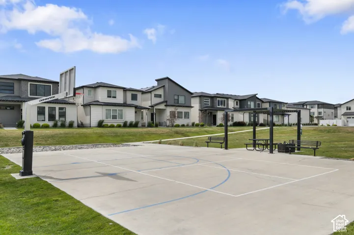 Outdoor recreational space featuring a concrete sports court with a basketball hoop, a shaded pergola with picnic tables and benches, and expansive green lawns