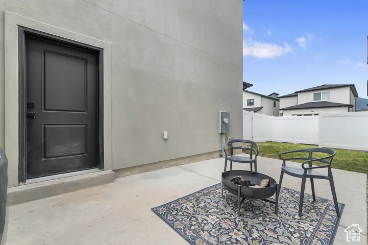 Concrete patio space featuring a solid panel exterior door, stucco wall finish, and a white vinyl privacy fence enclosing a grass area