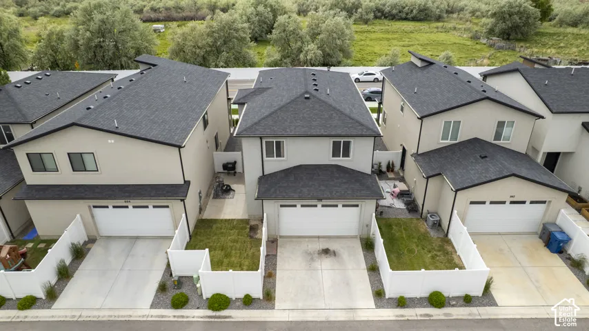 Modern stucco exterior featuring a dark asphalt shingle roof, attached two-car garage, and a fenced front yard with a concrete driveway