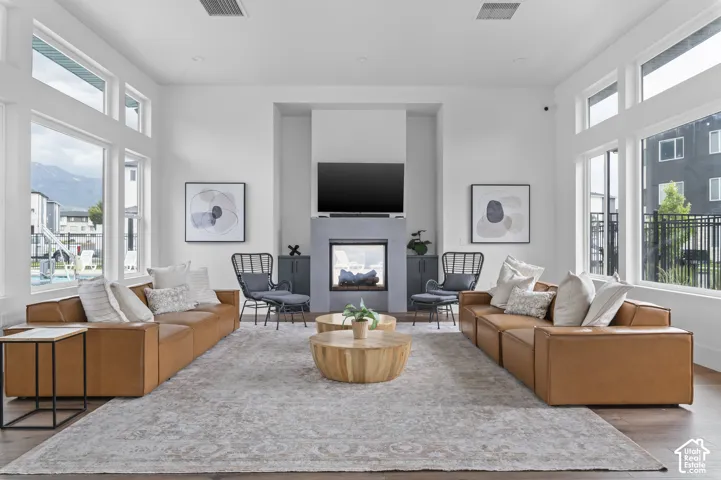 Spacious communal area featuring a modern fireplace, high ceilings, large windows, wood-finish flooring, and a decorative area rug