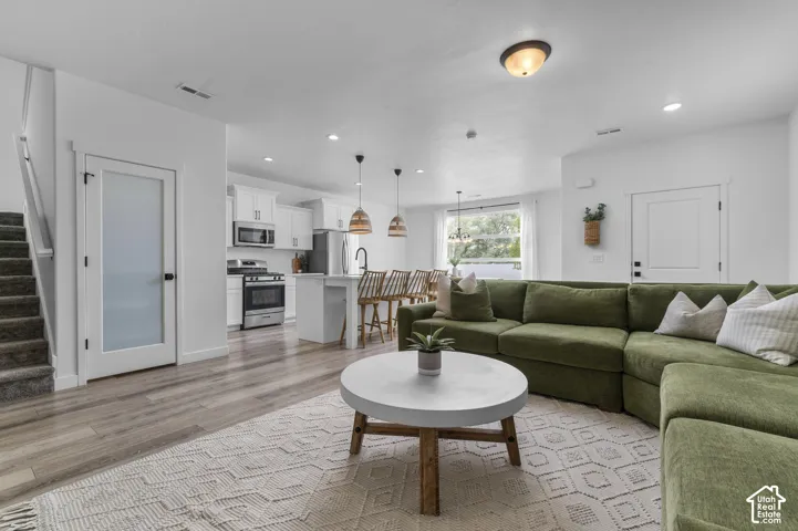 Open-concept living area featuring wood-finish flooring, white walls, and a modern kitchen with stainless steel appliances