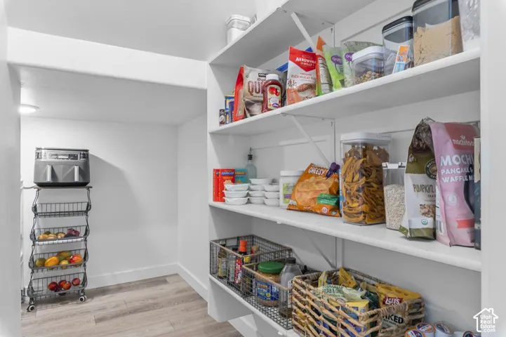 Walk-in pantry featuring expansive shelving, white walls, and wood-finish flooring