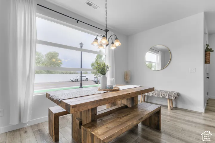 Dining area featuring large-pane windows with white framing, wood-finish flooring, a contemporary black chandelier, and crisp white walls
