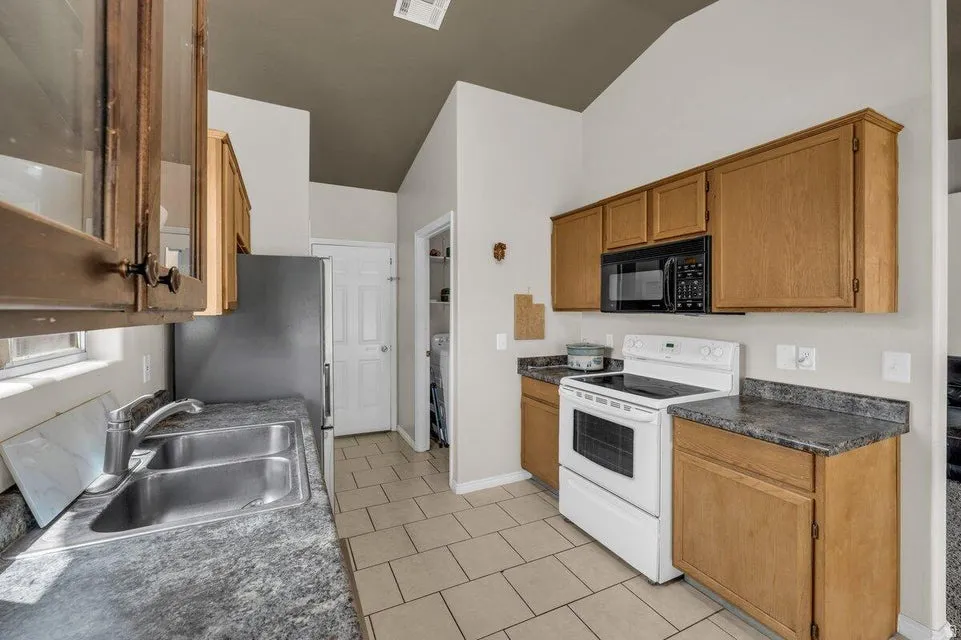 Kitchen featuring a double stainless steel sink, black microwave, white electric range, and light wood cabinetry with dark countertops