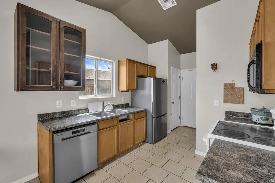 Kitchen featuring a vaulted ceiling, wood-finish cabinetry, stainless steel appliances, a double basin sink, and tile flooring