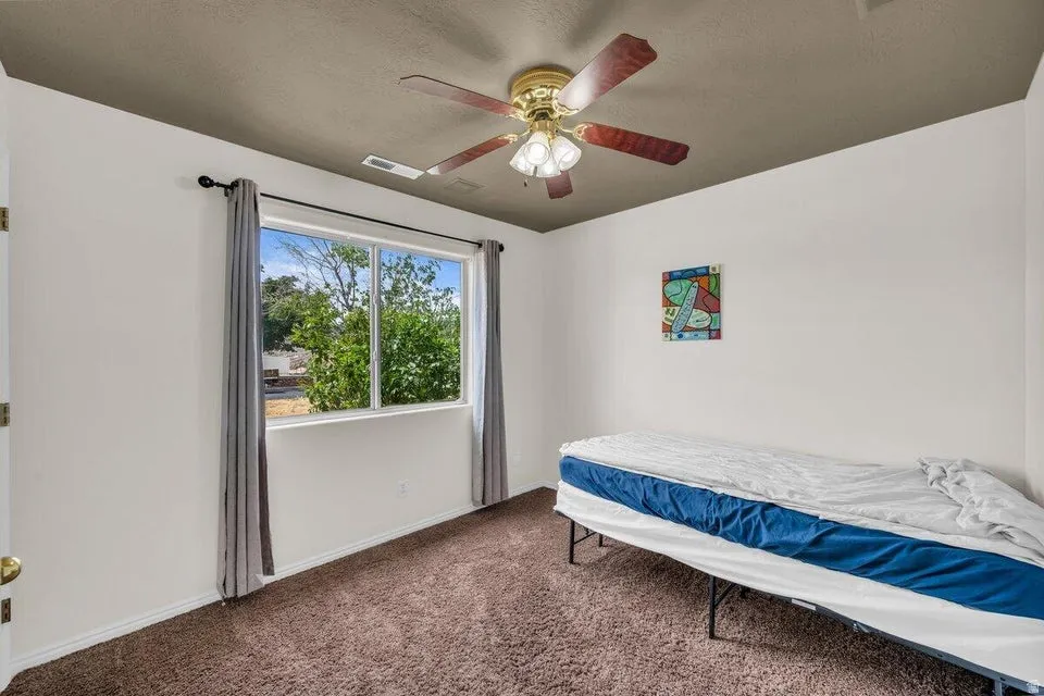 Bright room featuring a large window, brown carpet flooring, and a ceiling fan with integrated lighting