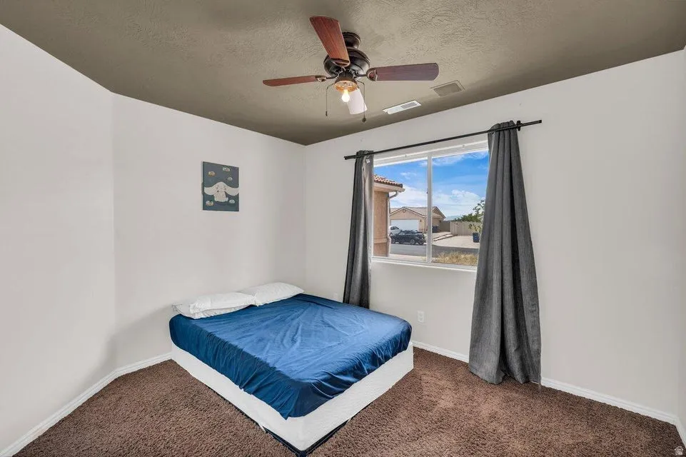 Bedroom featuring a window with a neighborhood perspective, a ceiling fan with light fixture, and brown carpeting
