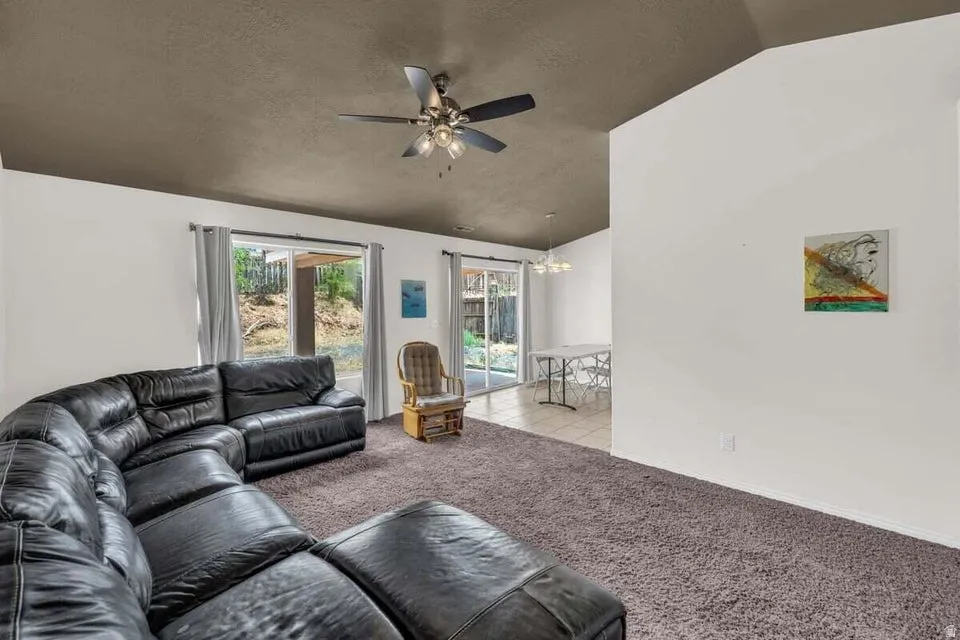 Spacious living area featuring vaulted ceilings, ceiling fan, and brown carpet flooring