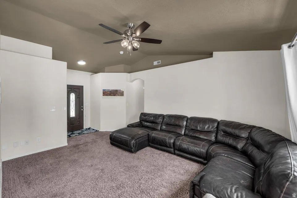 Carpeted living area featuring a vaulted ceiling with a ceiling fan