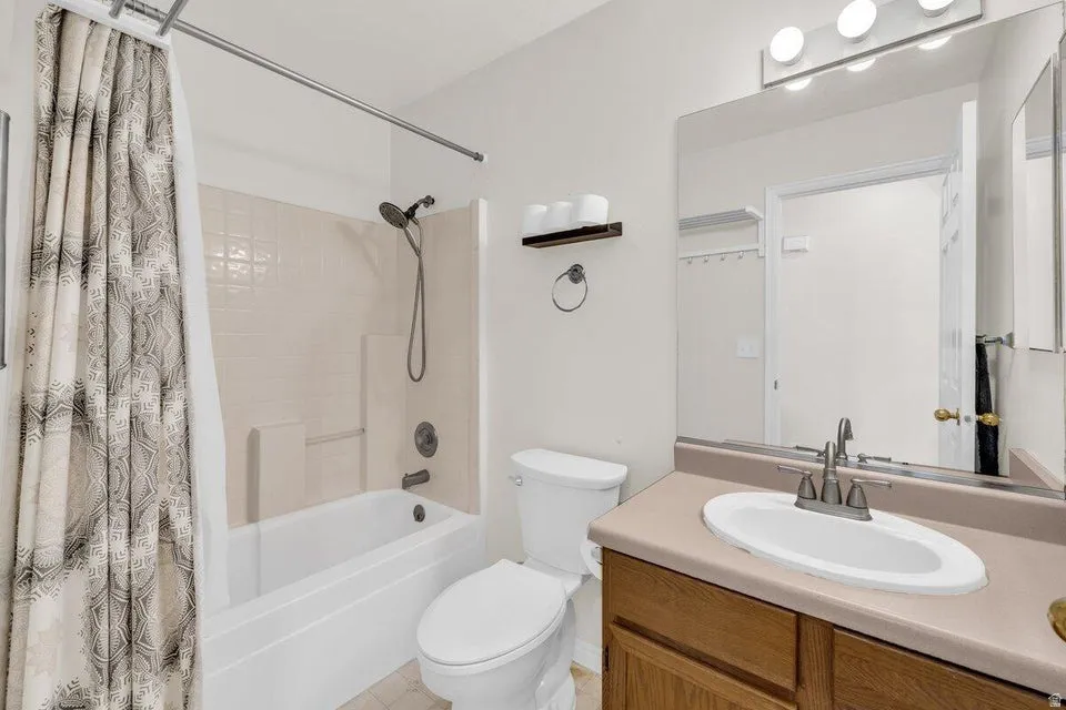 Full bathroom featuring a white tub-shower combination with tiled surround, a toilet, and a vanity with a drop-in sink and a large mirror