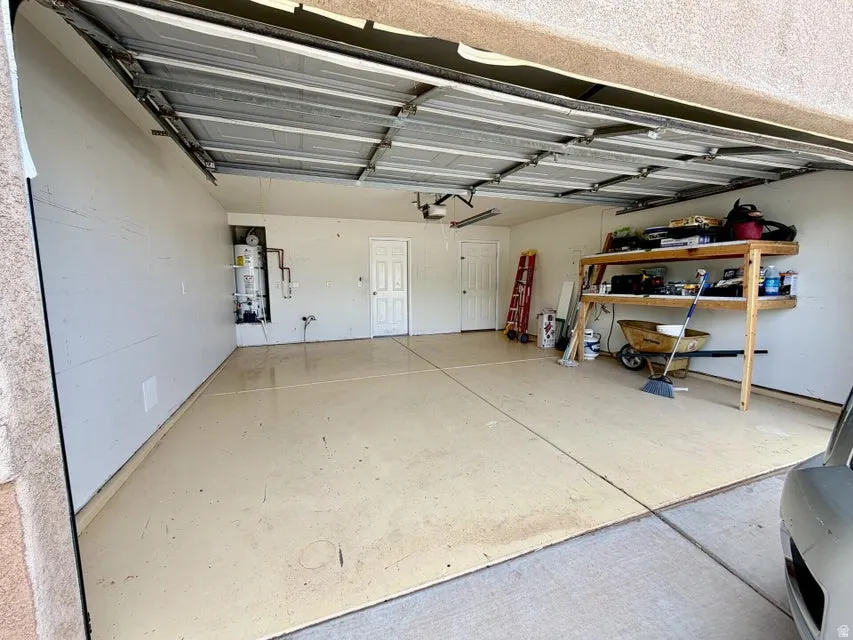 Two-car garage featuring an epoxy-coated concrete floor, an exposed ceiling with an automatic garage door opener, and a built-in water heater