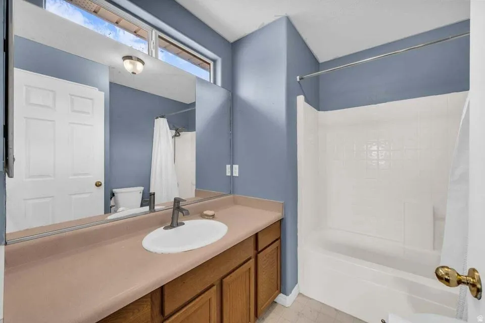 Bathroom featuring a single vanity with an oval basin, a bathtub with a shower, wood-finish cabinetry, and a full-width mirror
