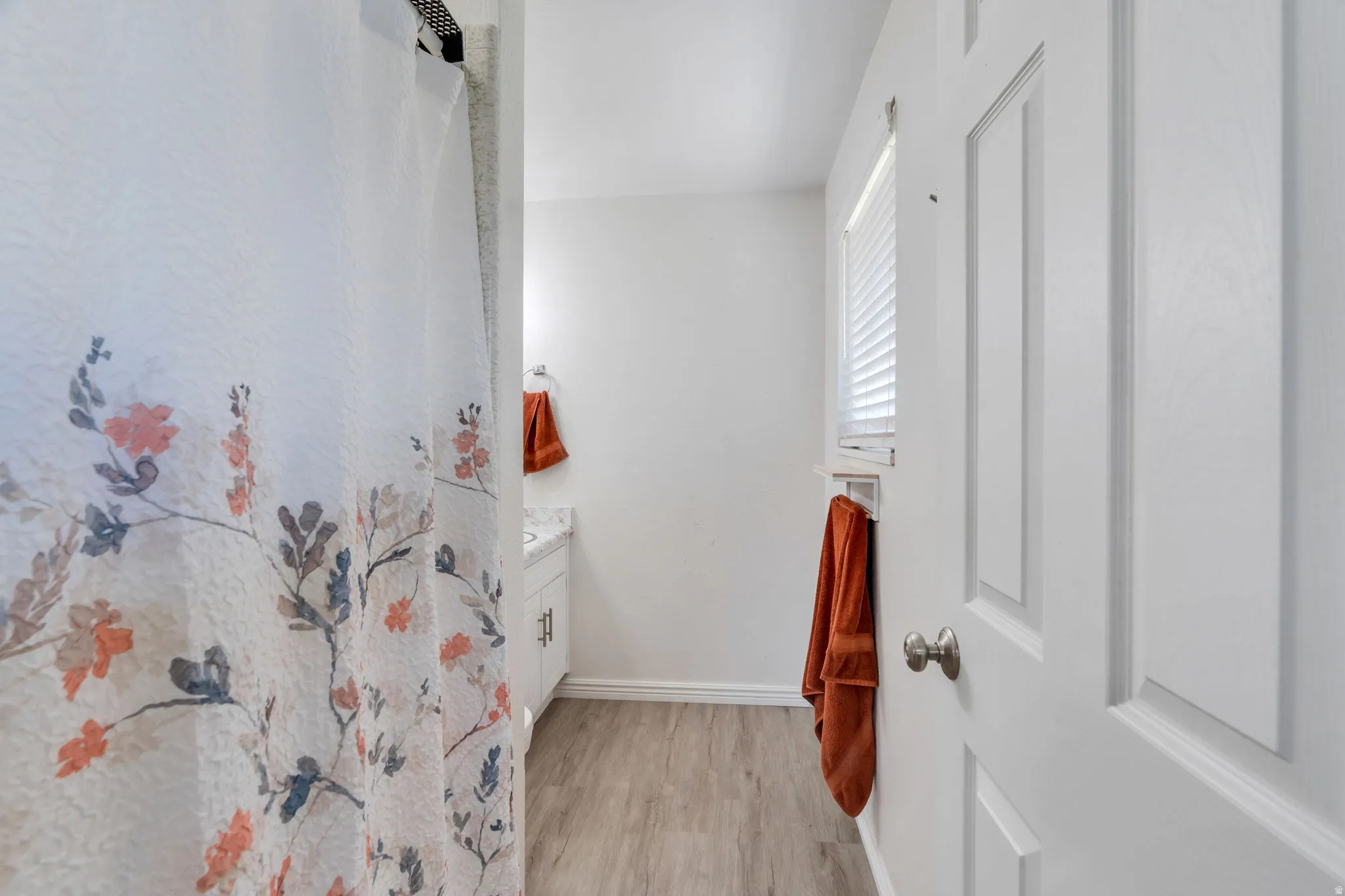 Primary bathroom featuring LVP flooring, a white vanity with a light-colored countertop, a window with blinds and shower