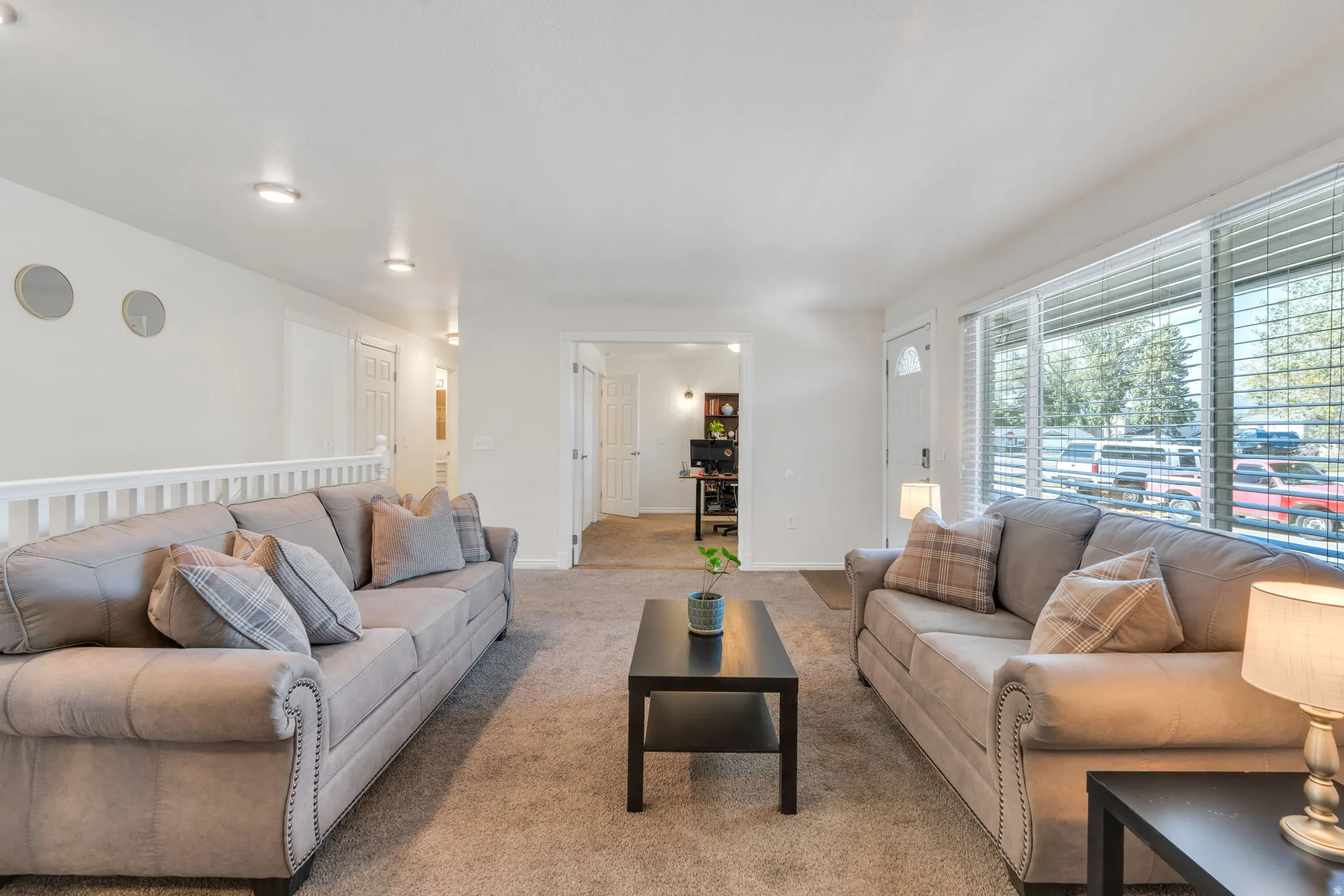 Carpeted living area featuring recessed lighting, large front window with blinds, and white interior doors
