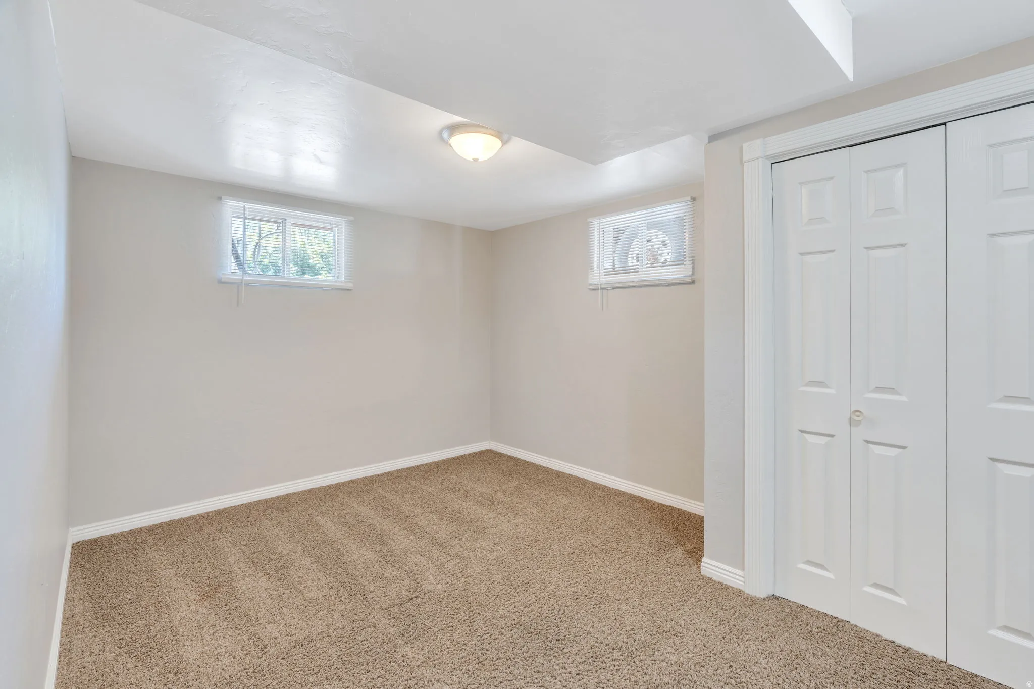 Apartment bedroom #1 with neutral-toned carpeting, two windows and a ceiling-mounted light fixture