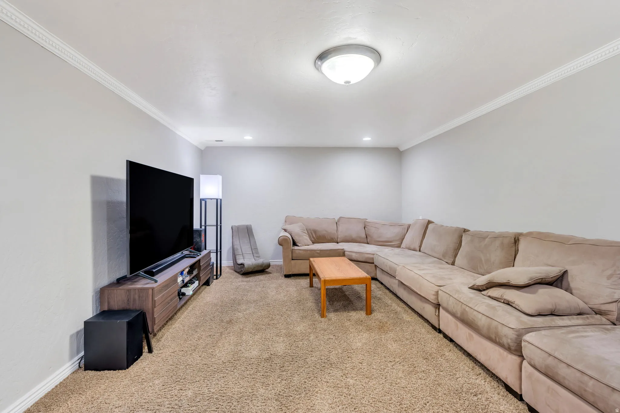 Carpeted basement family room with recessed lighting and crown molding